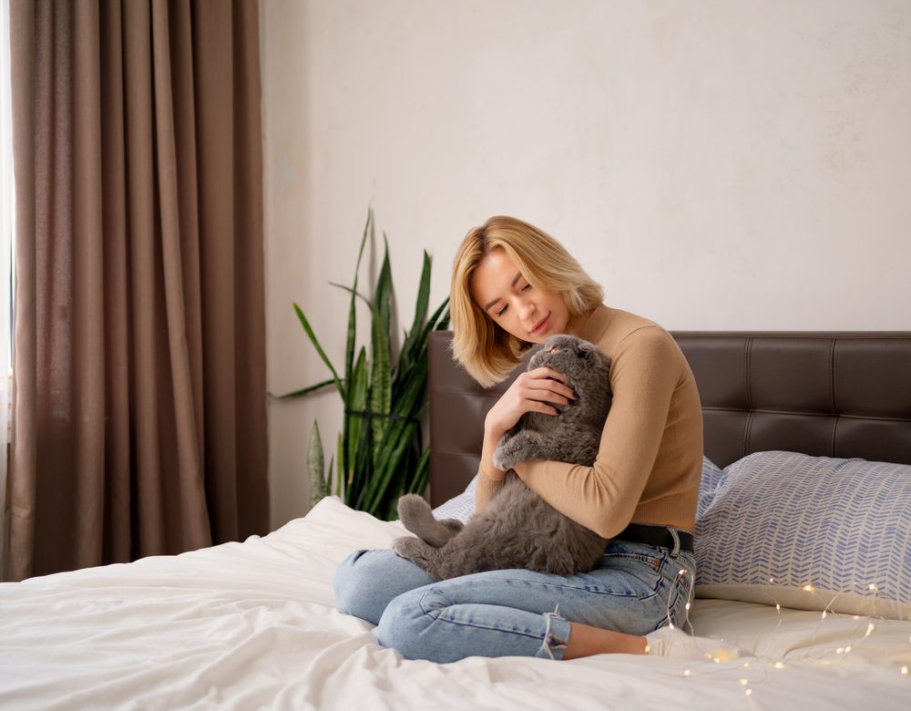 A customer sitting on her bed cuddling her grey cat