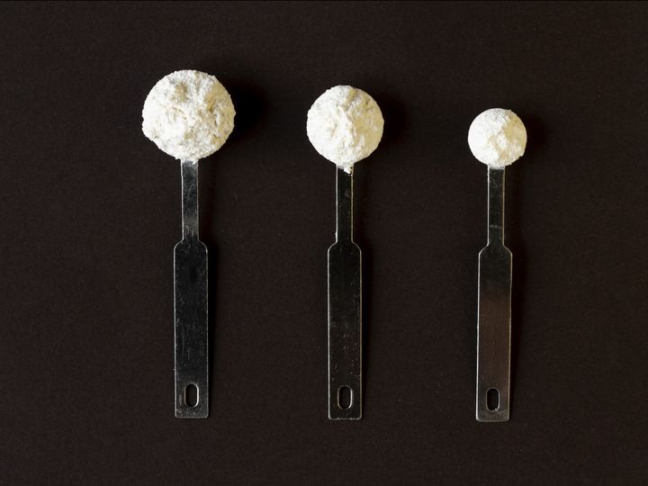 Three measuring spoons heaped with white powder, in graduated sizes